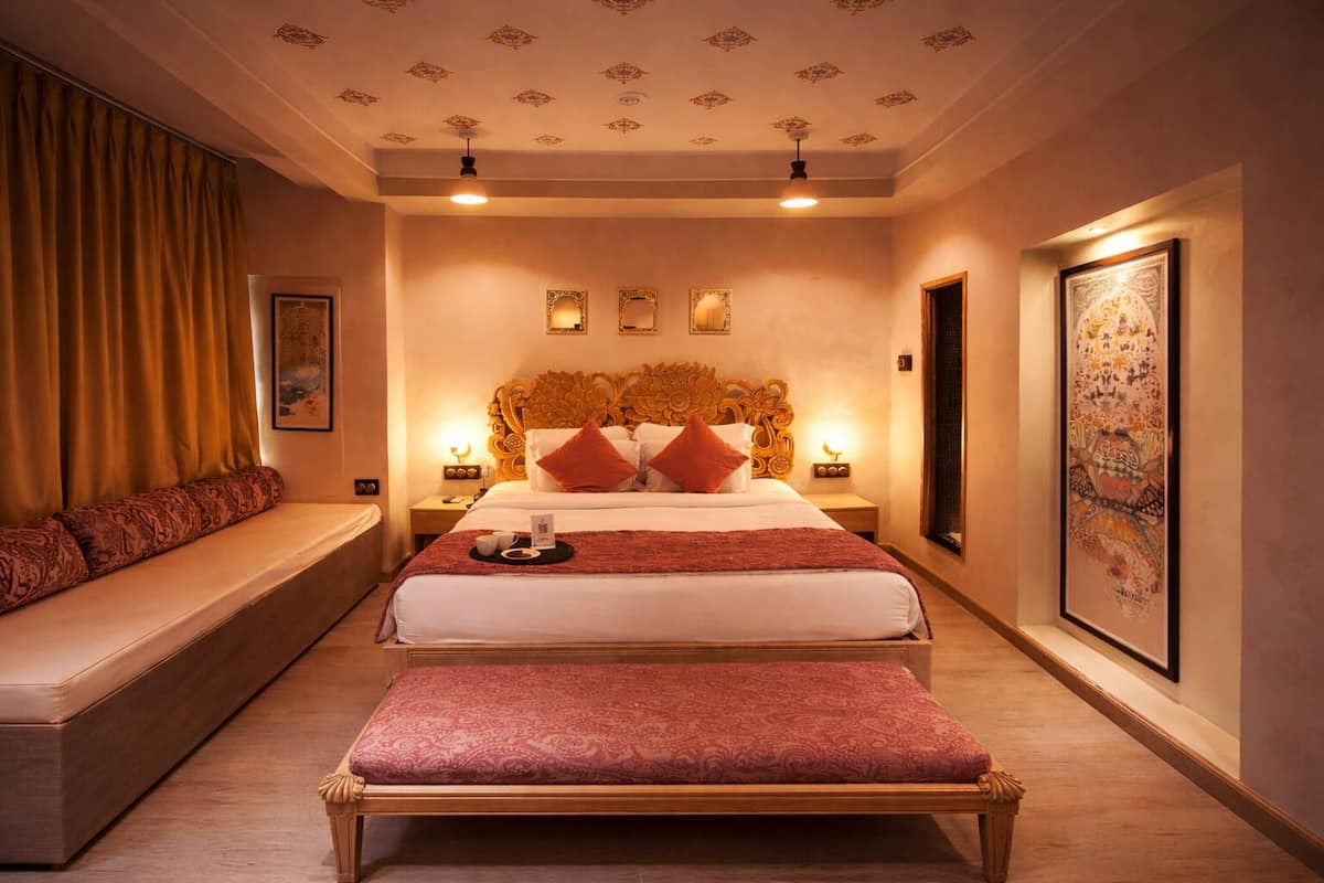 Una habitación de hotel con una cama grande, un banco, un sofá y una pared decorada con cuadros.