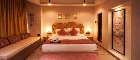 A hotel room with a large bed, a bench, a sofa, and a wall with framed artwork.