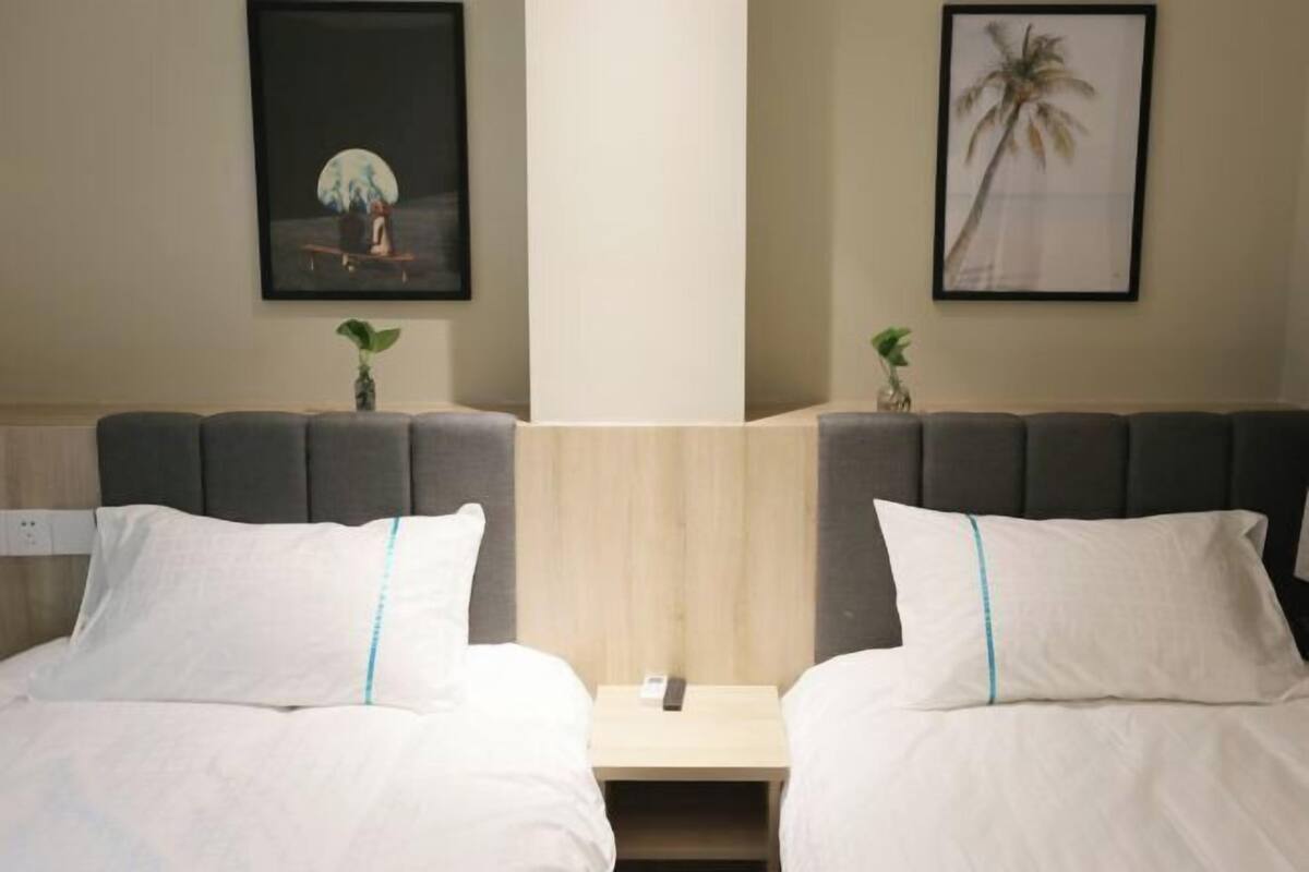 Habitación de hotel con dos camas, una mesita de noche y cuadros en las paredes.