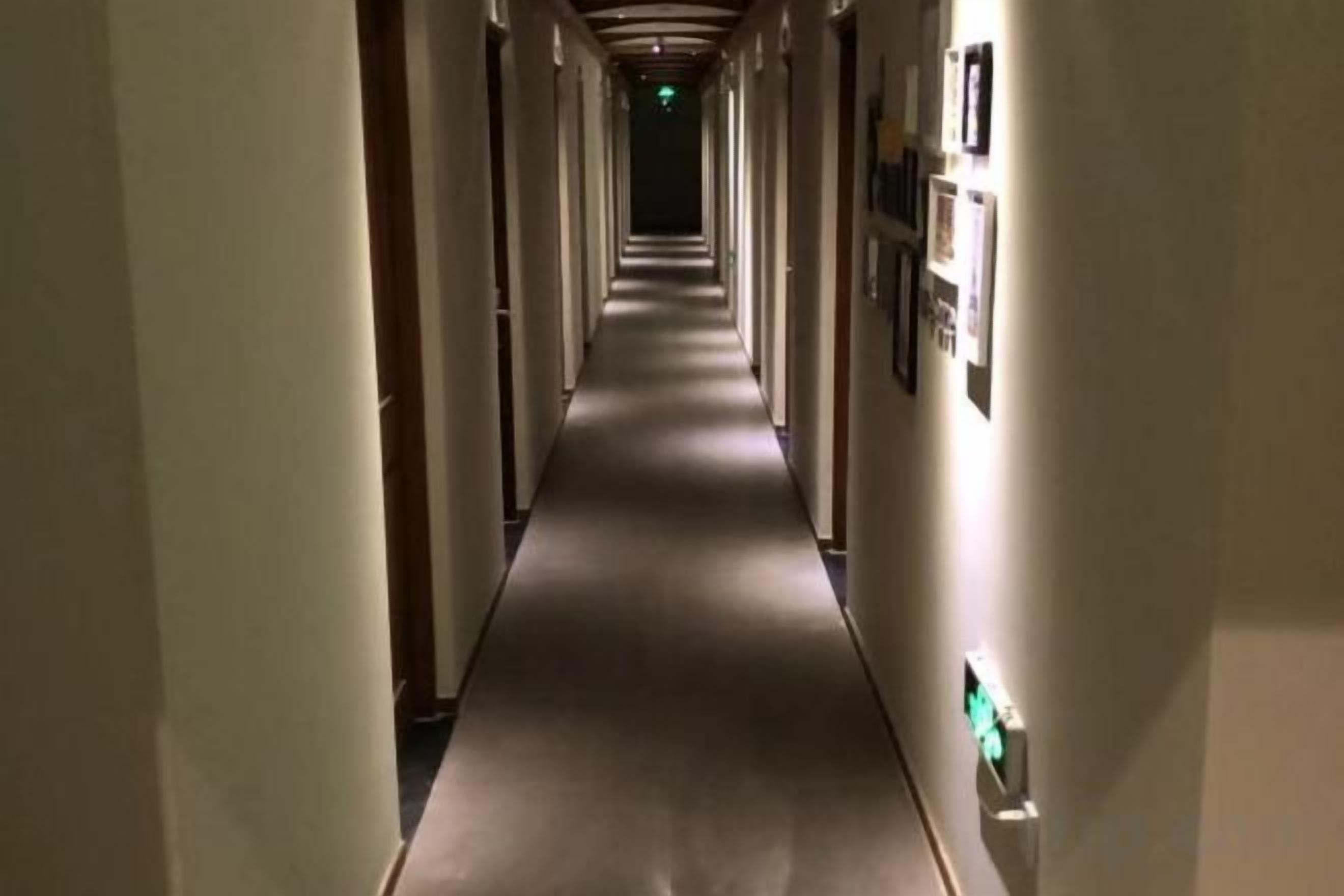Een lange, smalle hotelgang met deuren aan beide kanten en een vloerbedekking.