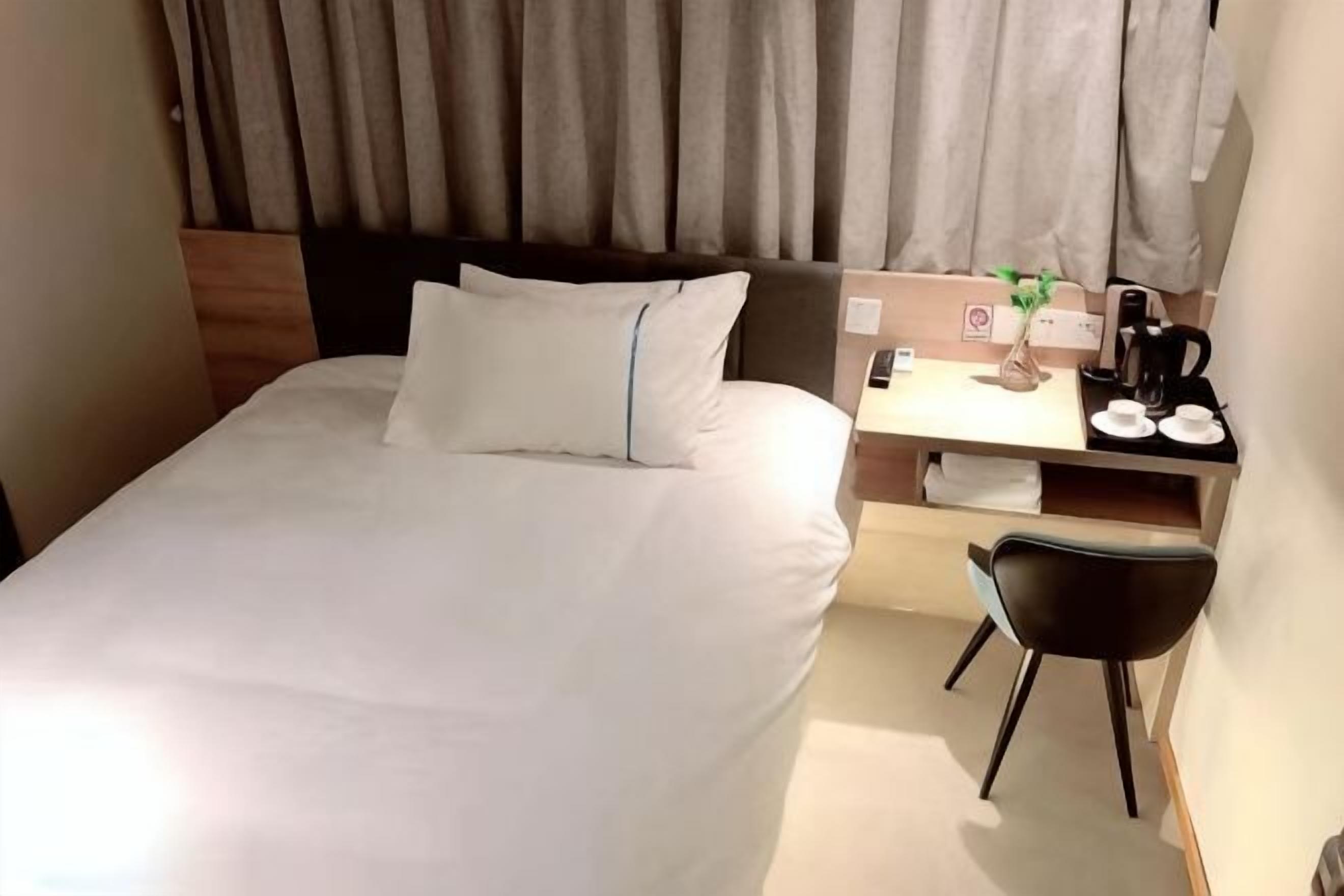 A hotel room with a bed, a desk with a chair, a coffee maker, and a small plant.
