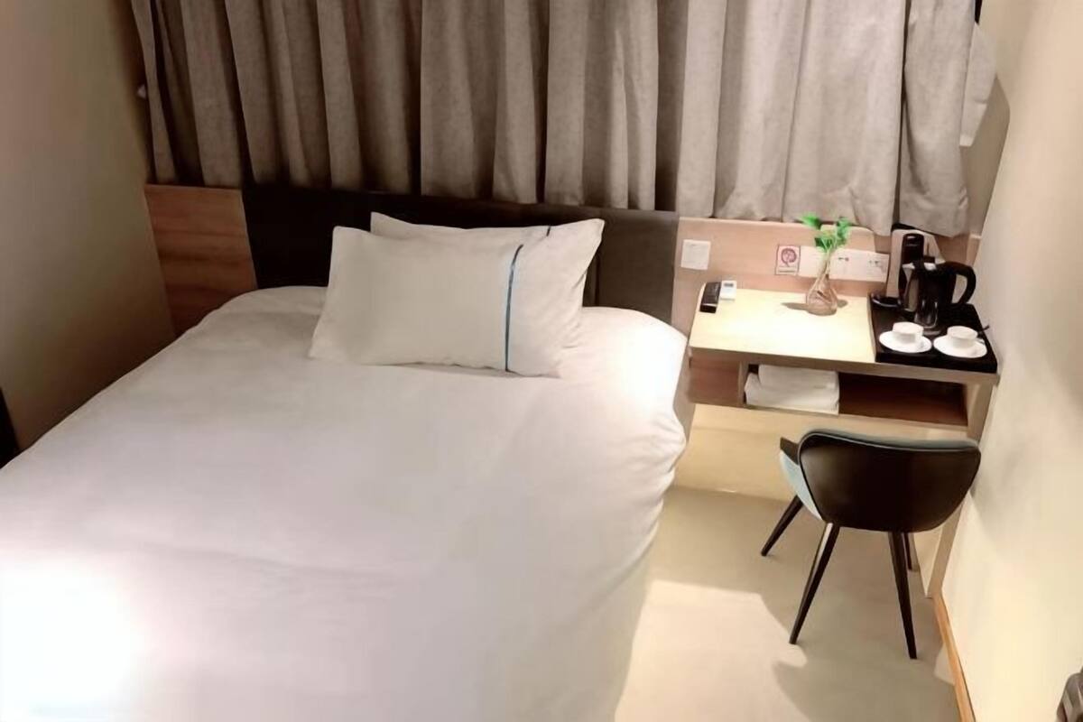 Una habitación de hotel con una cama, un escritorio con silla, una cafetera y una planta pequeña.