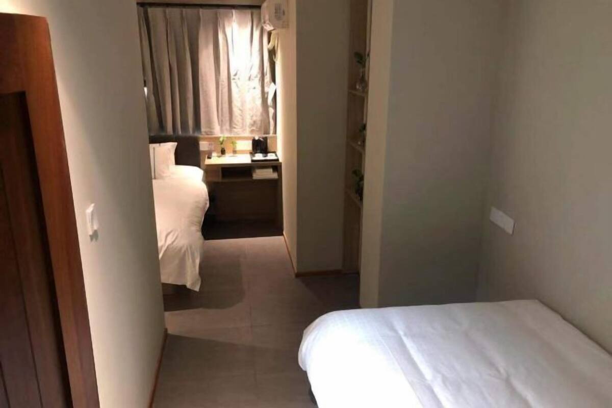 Un pasillo estrecho que conduce a un dormitorio con una cama, un escritorio con silla y una ventana con cortinas.
