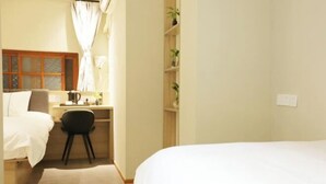 Quarto de hotel com cama, escrivaninha, cadeira e prateleira com plantas.