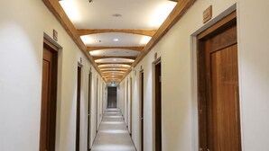 Um longo corredor com portas de madeira em ambos os lados, dando acesso a quartos individuais.