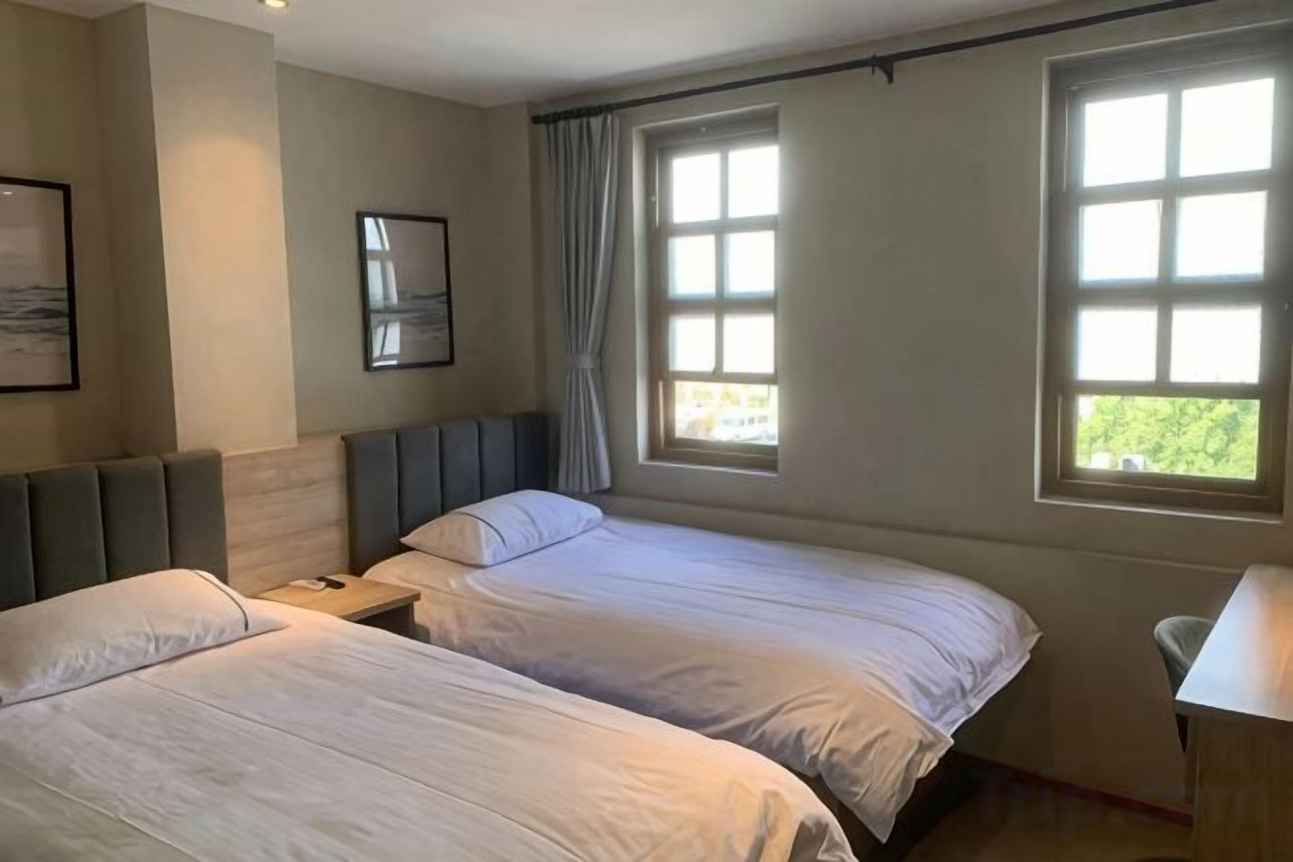 A hotel room with two beds, a desk, and a window with curtains.