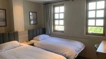 A hotel room with two beds, a desk, and a window with curtains.