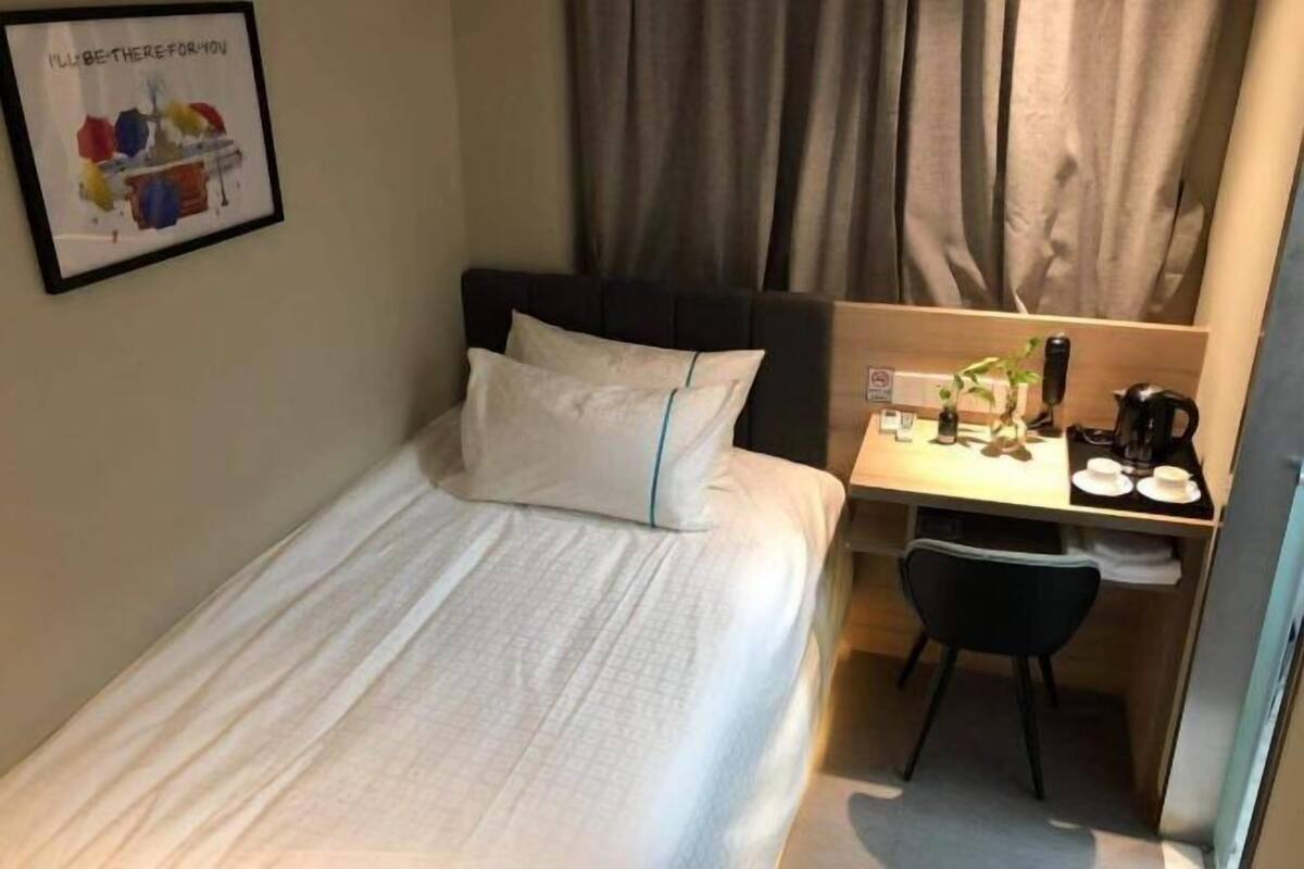 Una cama individual con cabecera, un escritorio con silla, una cafetera y un cuadro en la pared.
