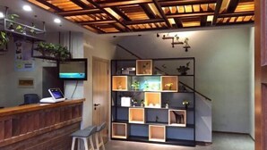 Uma área de recepção com balcão de madeira, laptop, televisão e escada com prateleiras.