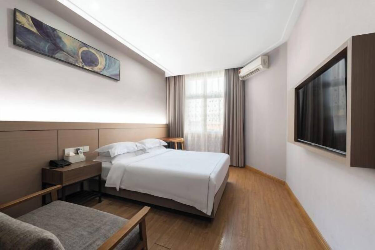 A hotel room with a bed, bedside table, lamp, and a painting on the wall.