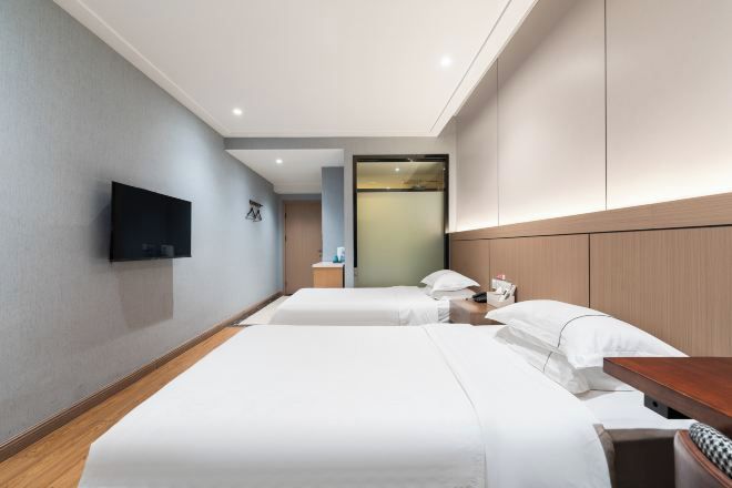 Habitación de hotel con dos camas, un televisor de pantalla plana montado en la pared, una mesita de noche con lámpara y un espejo grande sobre la cabecera.