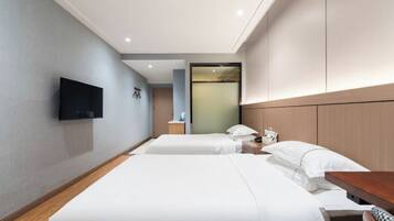 Habitación de hotel con dos camas, un televisor de pantalla plana montado en la pared, una mesita de noche con lámpara y un espejo grande sobre la cabecera.