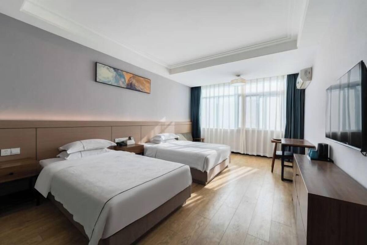 A hotel room with two beds, a desk, a chair, a TV, and a painting on the wall.