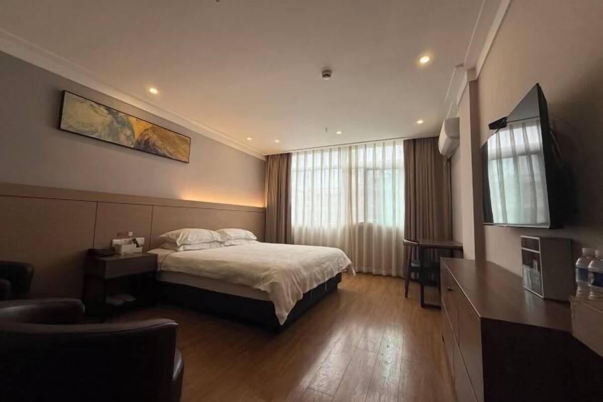 A hotel room with a bed, bedside table, chair, TV, and a painting on the wall.