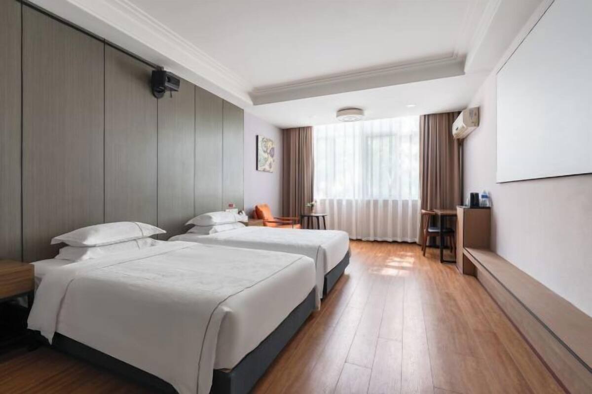 A hotel room with two beds, a desk, a chair, and a large window with curtains.