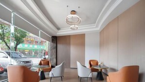 Un interior moderno con zona de comedor que presenta mesas y sillas redondas, una lámpara de techo original y grandes ventanales con vistas a la calle.