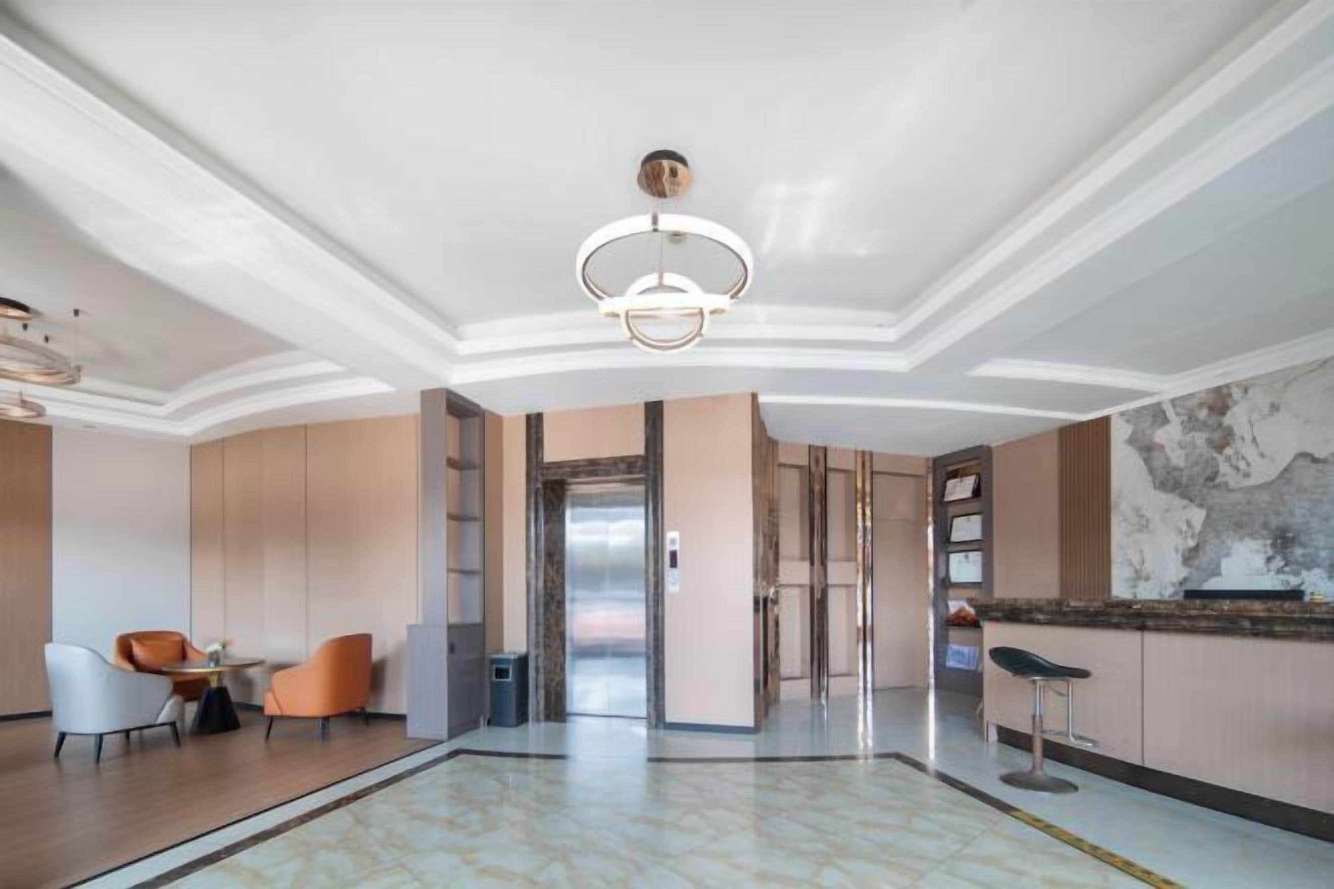 Un vestíbulo amplio con piso de mármol, un candelabro moderno y un mostrador de recepción.