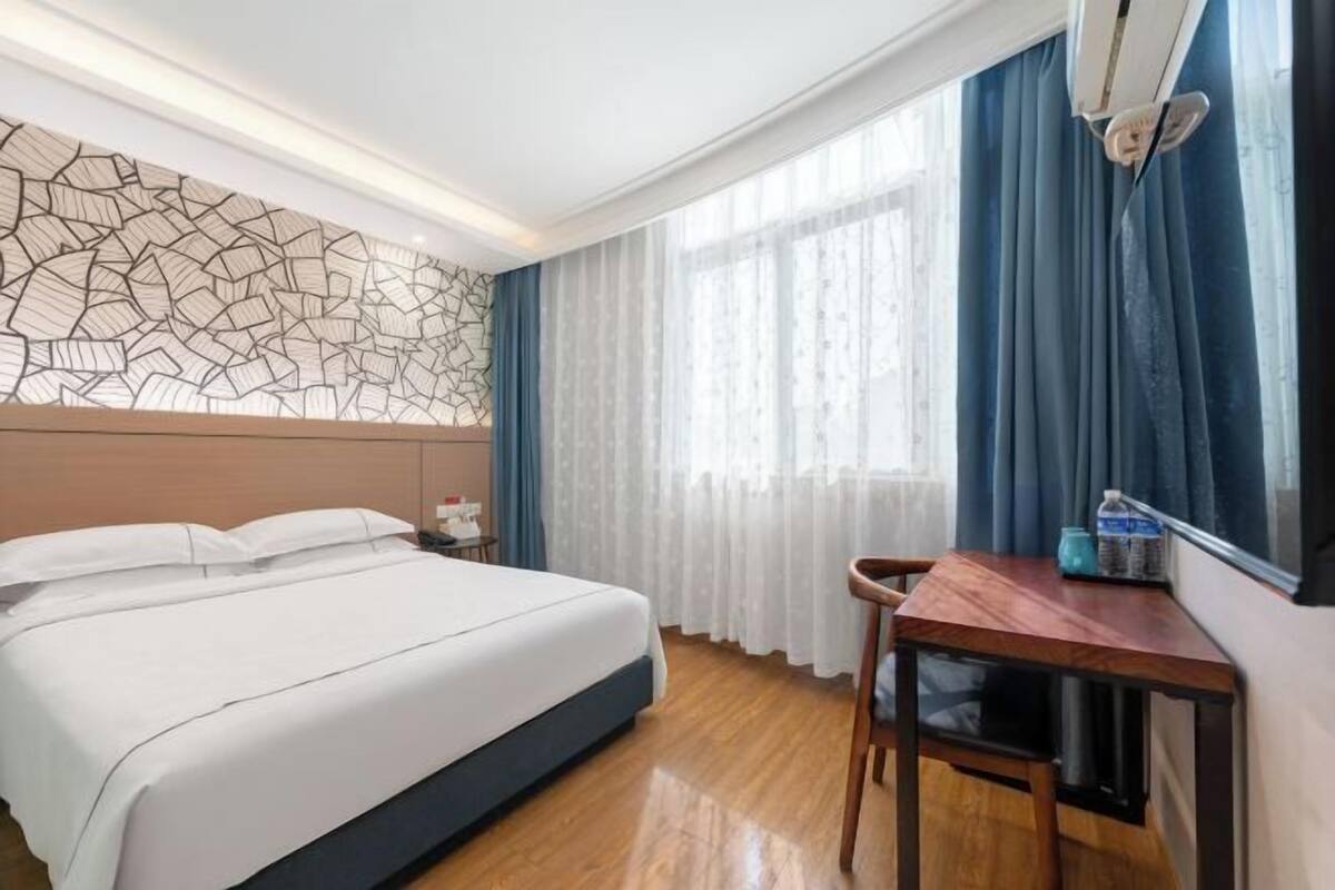 A hotel room with a bed, a desk, a chair, a window with curtains, and a decorative wall panel.