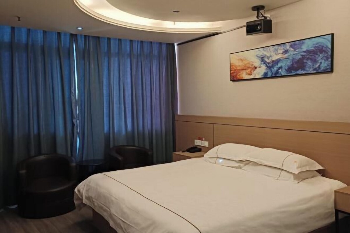 A hotel room with a bed, a desk, a chair, and a painting on the wall.