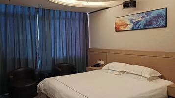 A hotel room with a bed, a desk, a chair, and a painting on the wall.
