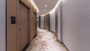 Un pasillo moderno de hotel con puertas de madera, una pantalla digital y una alfombra estampada.