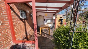 A brick building with a wooden table and chairs under a red-framed pergola. - Vacation apartment Dörpschipper in the smallest warf village of the Krummhörn (Krummhörn)