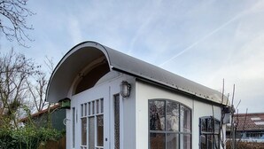 A small, white, single-story house with a curved roof, a front door, and a small porch. - Vacation apartment Dörpschipper in the smallest warf village of the Krummhörn (Krummhörn)