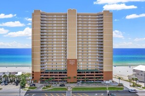 A high-rise hotel with multiple balconies, a beach view, and a parking area.