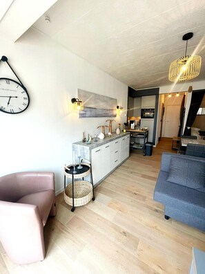 A modern living room with a sofa, a chair, a dining area with a table, and a kitchen in the background.