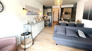 A modern living room with a grey sofa, a small dining table, and a kitchen area in the background. - Apartment Near Boat Club in Middelkerke (Middelkerke)