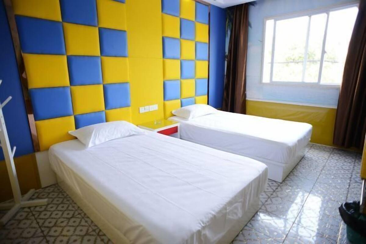 A room with two beds, a window with curtains, and a patterned floor.