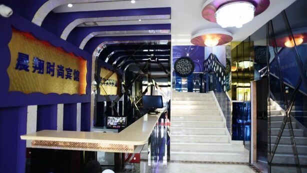 A modern interior with a staircase leading to upper levels, a reception desk, and a wall with a sign. - Chenxiang Fashion Hostel (Shanghai)