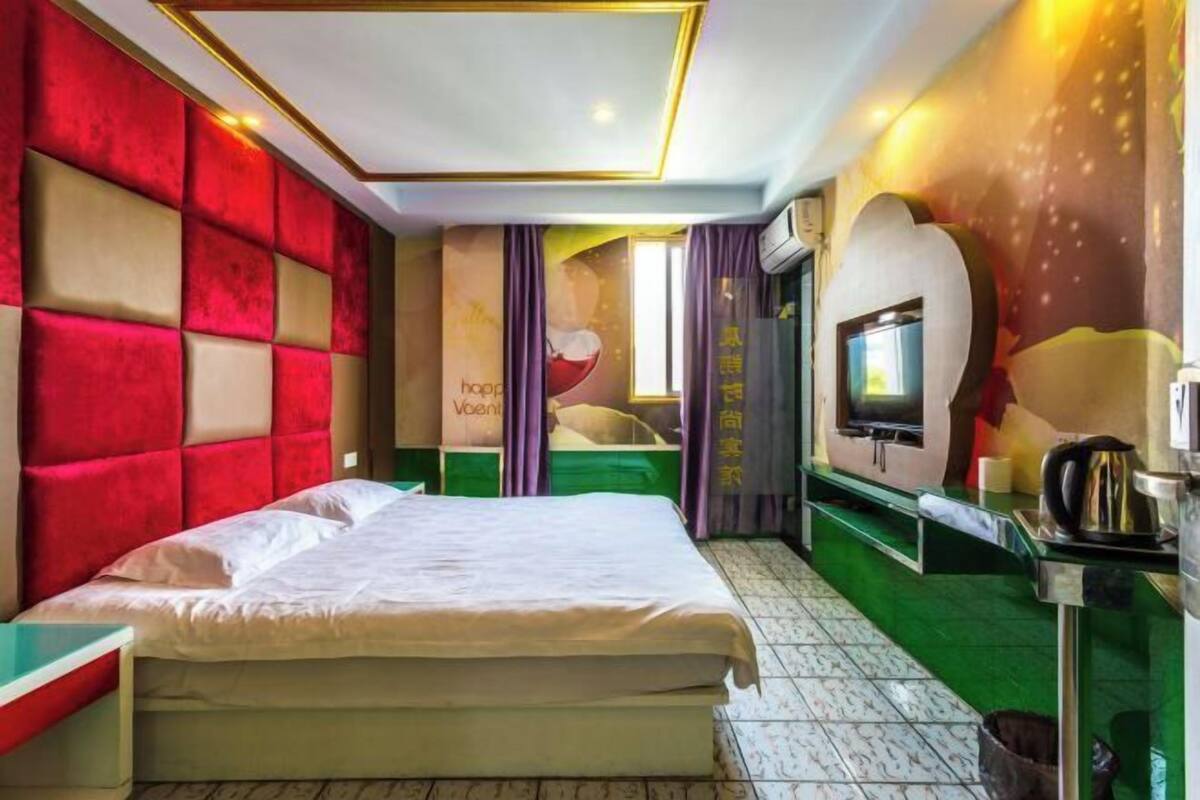 A hotel room with a large bed, a television, a minibar, and a green carpet.