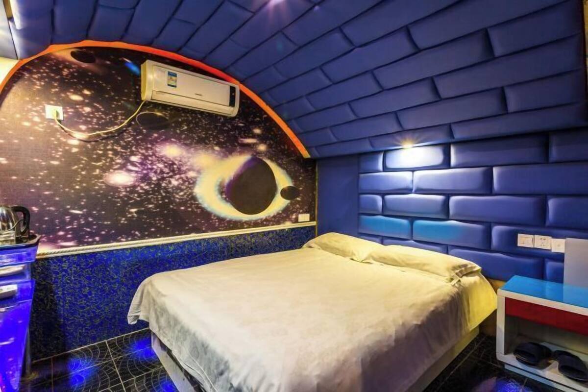 A room with a bed, a wall-mounted air conditioner, a shelf with shoes, and a wall with a space-themed mural.