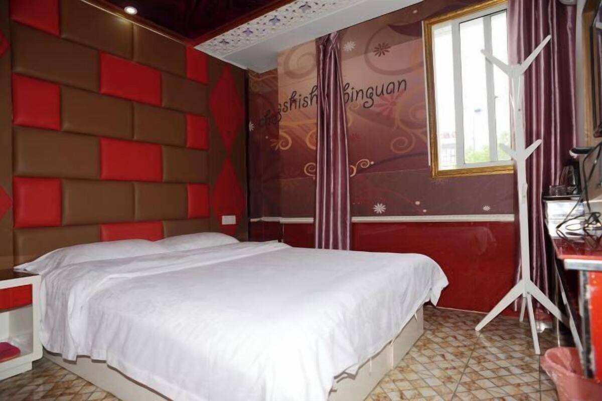 A hotel room with a bed, a desk, and a window with curtains.