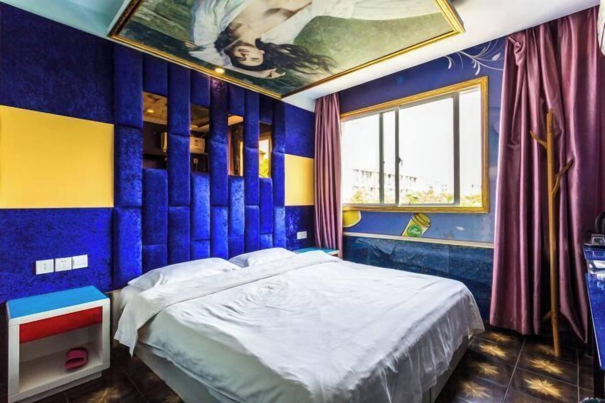 A bedroom with a bed, a nightstand, a window with curtains, and a ceiling mural.
