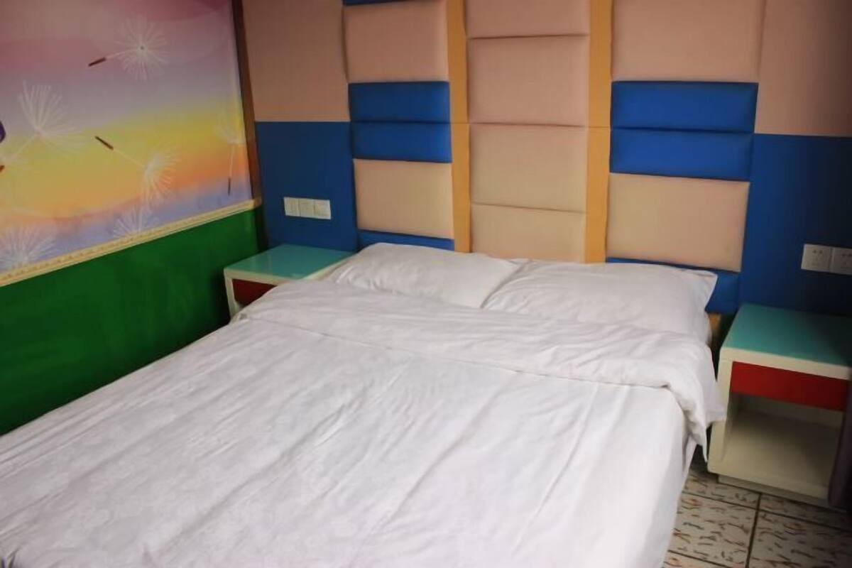 A bed with white bedding in a room with a colorful headboard and a green wall.