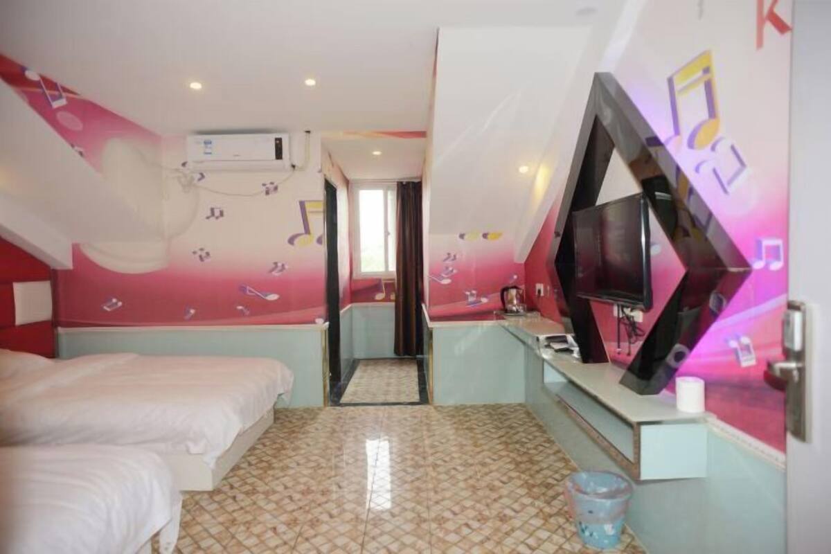 A hotel room with two beds, a TV, a mirror, and a bathroom visible through an open door.