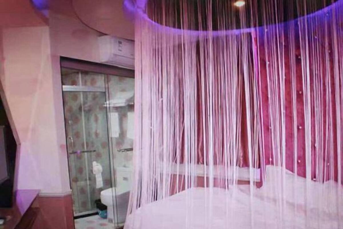 A room with a bed, a glass shower enclosure, and a purple-lit ceiling.