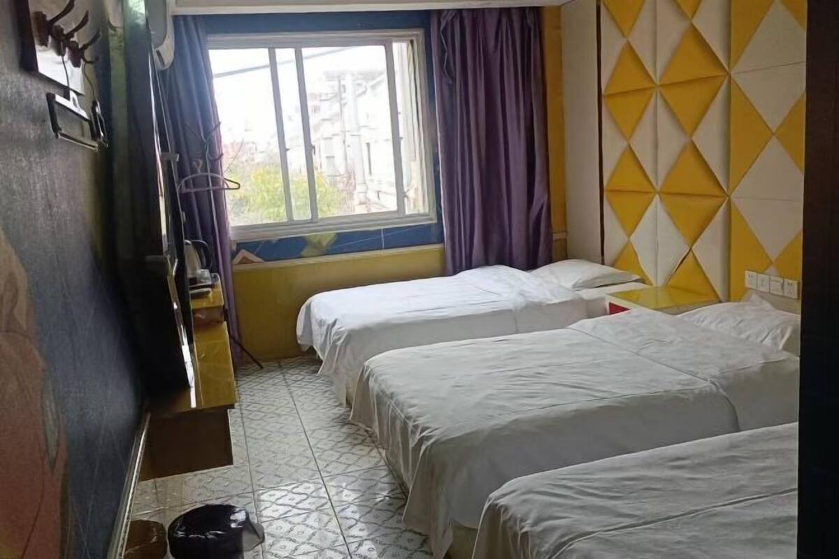 A hotel room with two beds, a window with curtains, a wall with a geometric pattern, and a tiled floor.