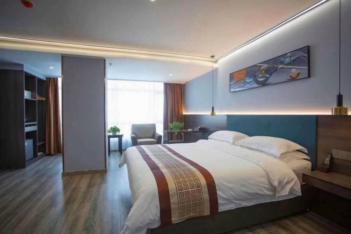 A modern hotel room with a large bed, a desk, and a view of the hallway.