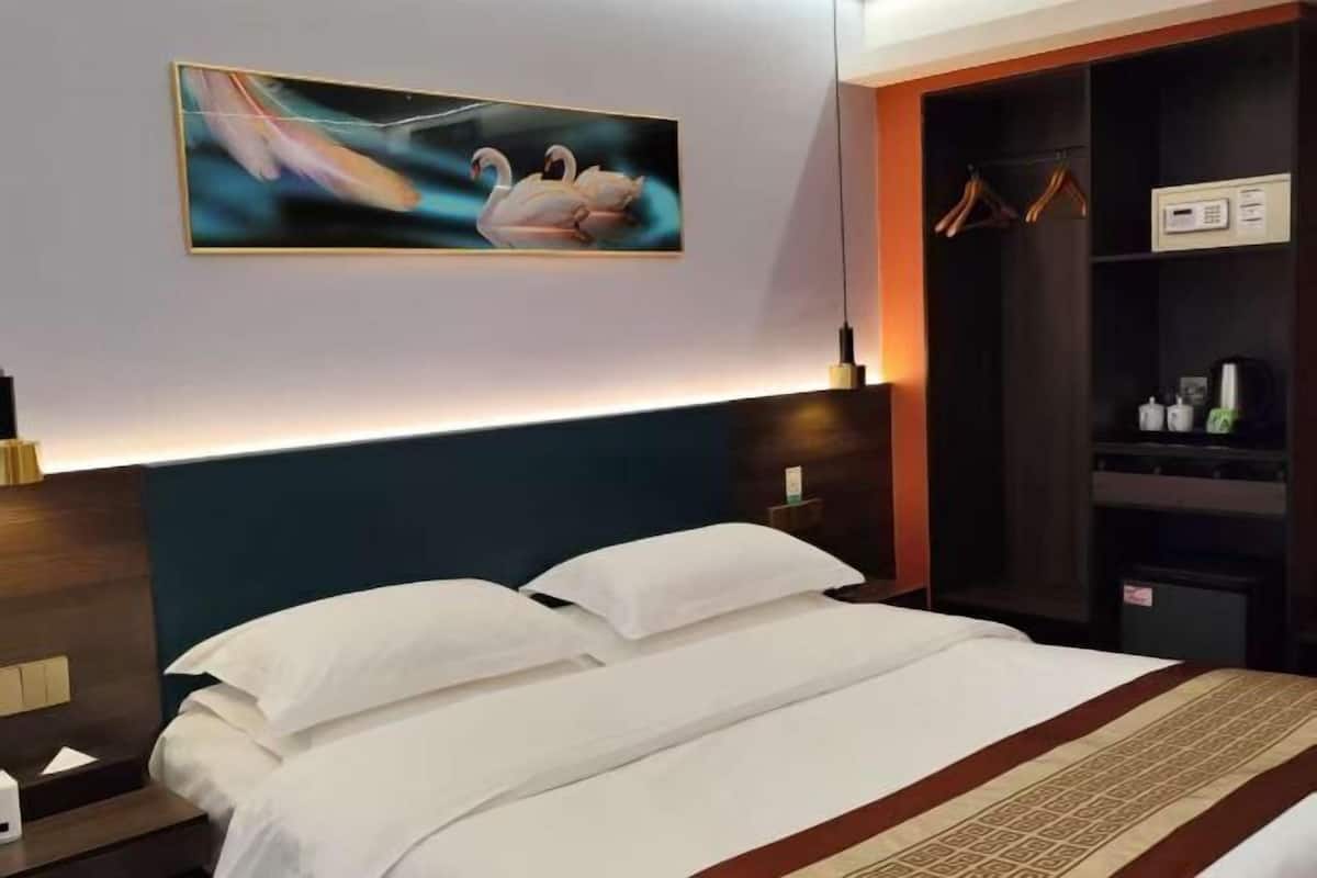 Una habitación de hotel con cama, cabecera, un cuadro colgado en la pared, armario y mesita de noche.