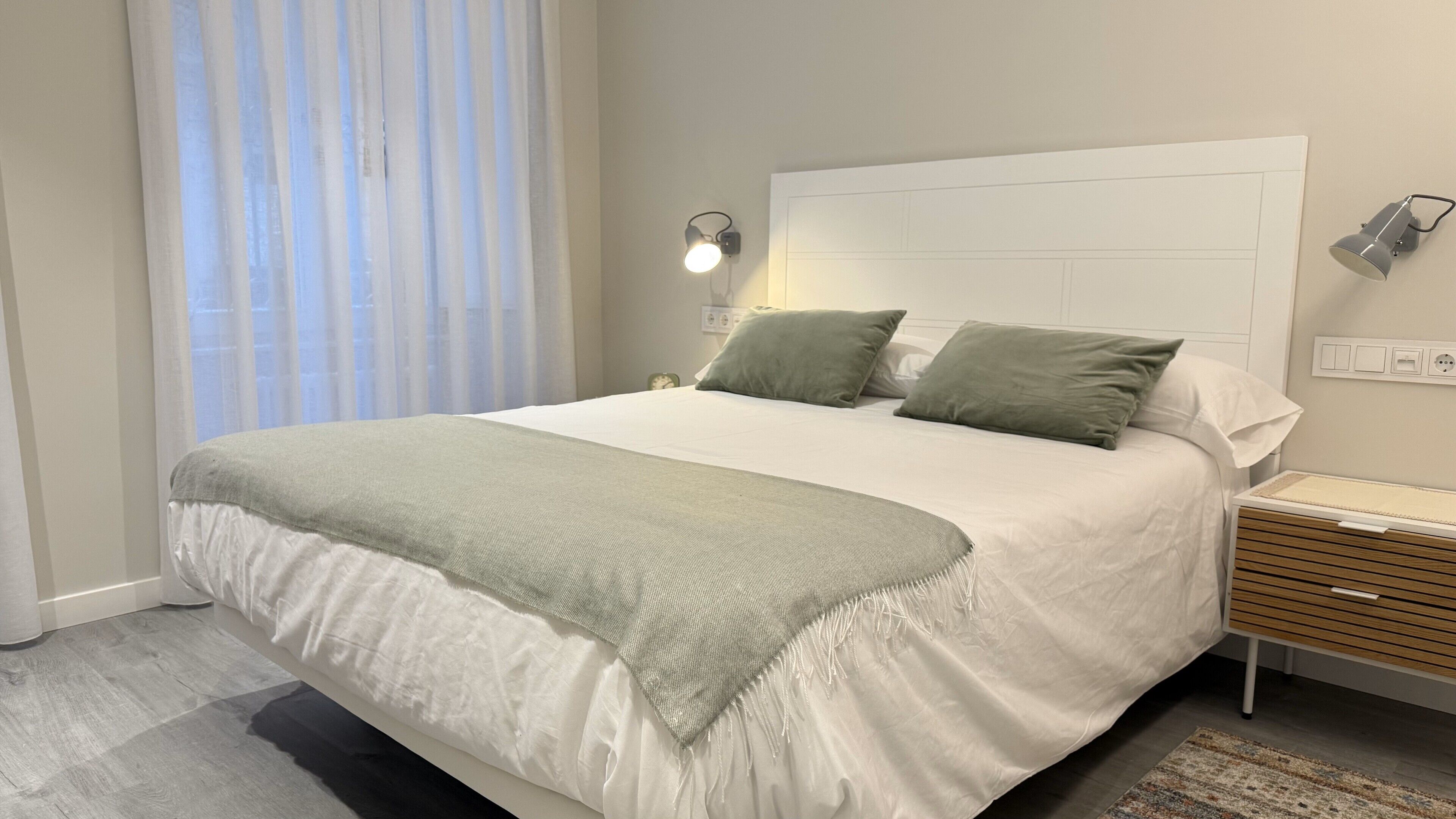 A neatly made bed with a white and green bedspread, two pillows, and a bedside table with a lamp.