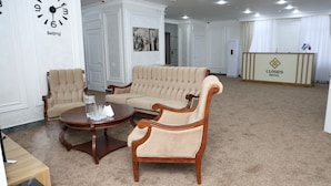 Eine Hotellobby mit einem beigefarbenen Sofa, zwei Sesseln, einem runden Holztisch und einem Empfangsschalter mit der Aufschrift "Clouds Hotel".