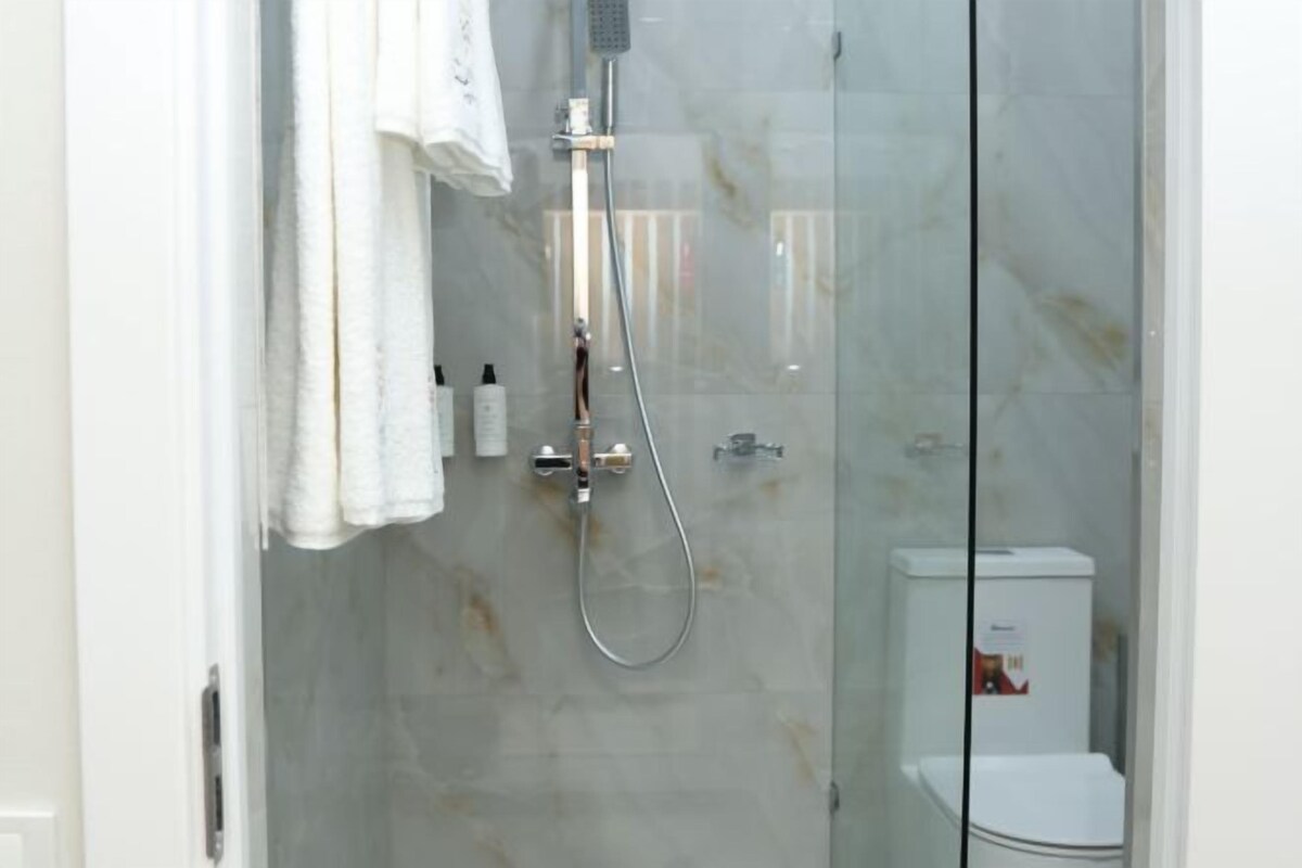 Ducha envuelta en vidrio, con cabezal de ducha de mano y grifo de pared.