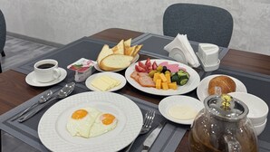 Ein Frühstückstisch mit verschiedenen Speisen, darunter Eier, Toast, Käse und Obst. An der Wand ist ein Fernseher angebracht, der Essensbilder zeigt.