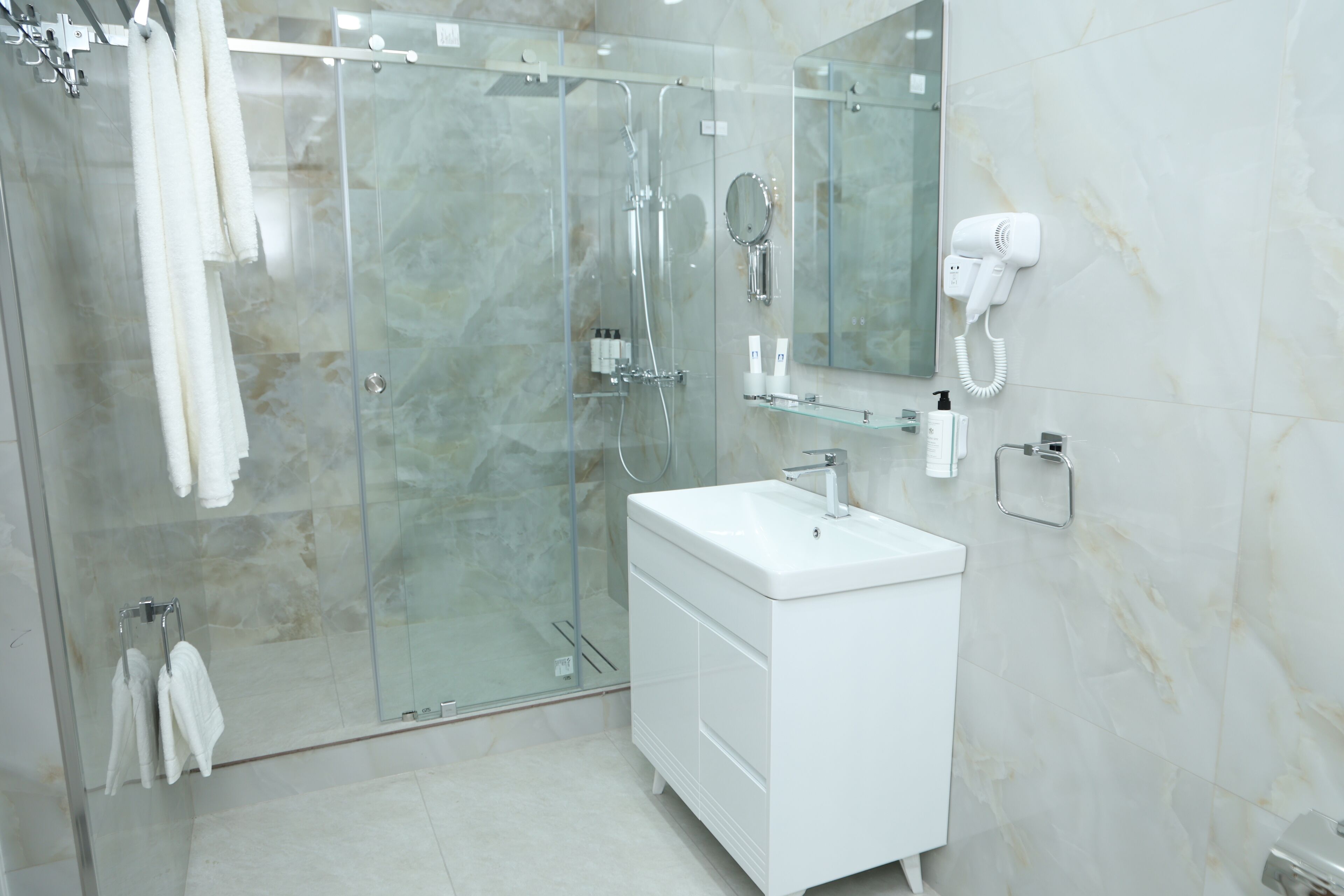 A modern bathroom with a glass-enclosed shower, a white vanity, and a mounted hairdryer.