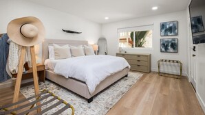 Un dormitorio con cama, mesitas de noche, armario, espejo y perchero.