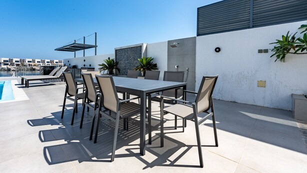 Un patio exterior con piscina, una mesa con sillas y un edificio moderno al fondo.