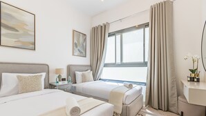 Habitación de hotel con dos camas, un escritorio, una ventana con cortinas y obras de arte en las paredes.